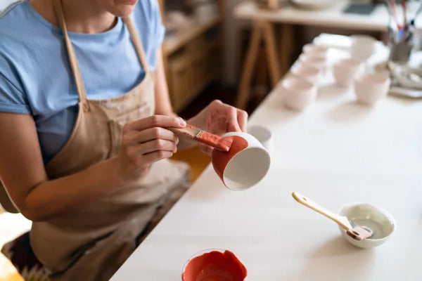 Handwerker bemalt eine Kermaiktasse mit roter Farbe