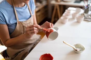 Handwerker bemalt eine Kermaiktasse mit roter Farbe